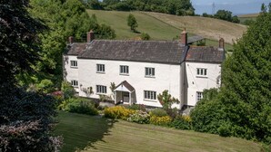 A white two-story house with a gabled roof, surrounded by lush greenery and a well-maintained lawn. - Pardlestone Farm – Self-Catering Cottages (Bridgwater)