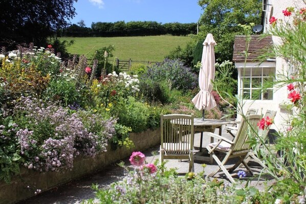 A garden patio with a table and chairs, surrounded by a variety of flowers and plants. - Pardlestone Farm – Self-Catering Cottages (Bridgwater)