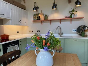 A kitchen with a wooden table, a white pitcher with flowers, and a hanging light fixture. - Pardlestone Farm – Self-Catering Cottages (Bridgwater)