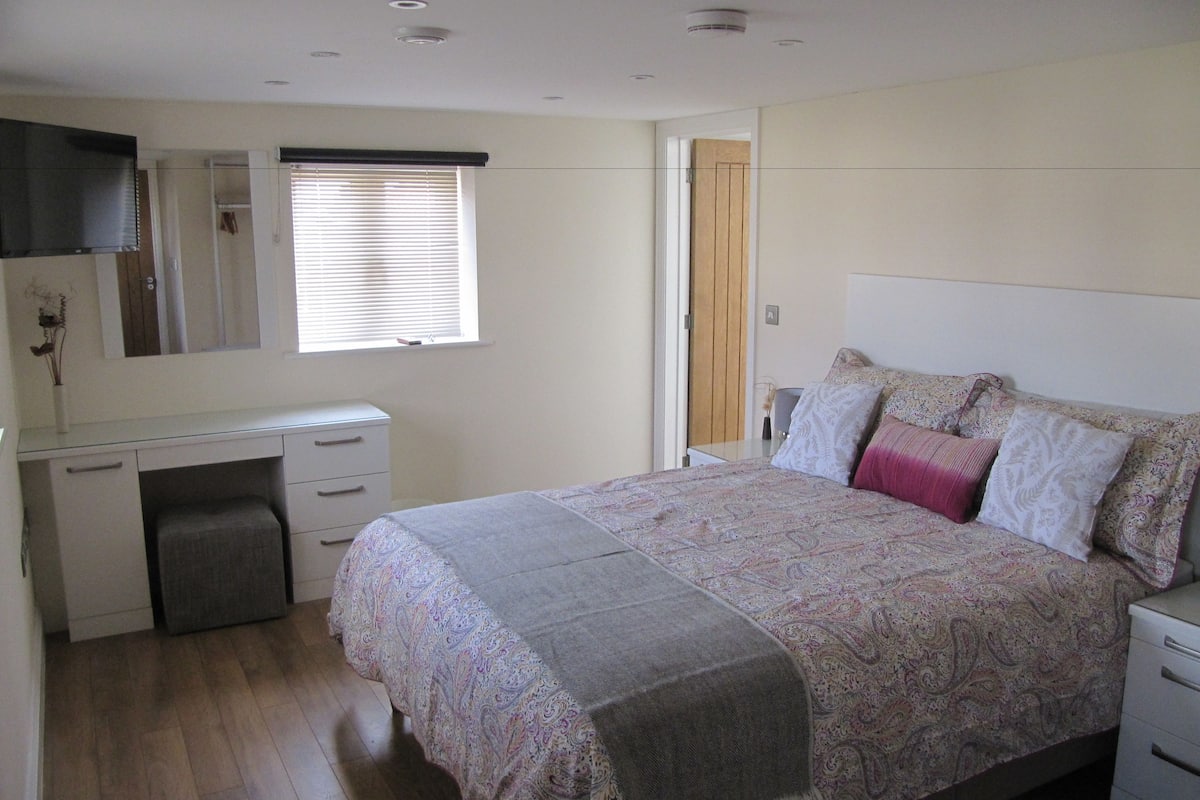 A bedroom with a bed, a desk, a chair, a wardrobe, a mirror, and a window with blinds.