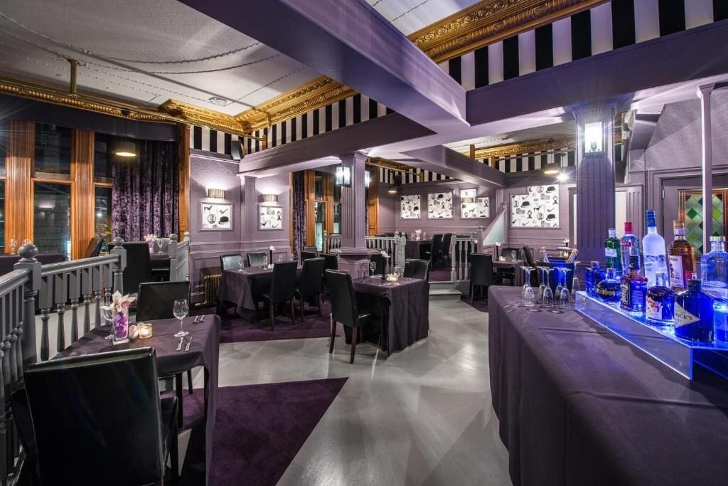 Un restaurante con mesas y sillas, una zona de bar con botellas y cuadros en las paredes.