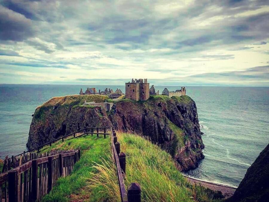 Un castillo costero en un acantilado con un sendero de madera que lleva a él.