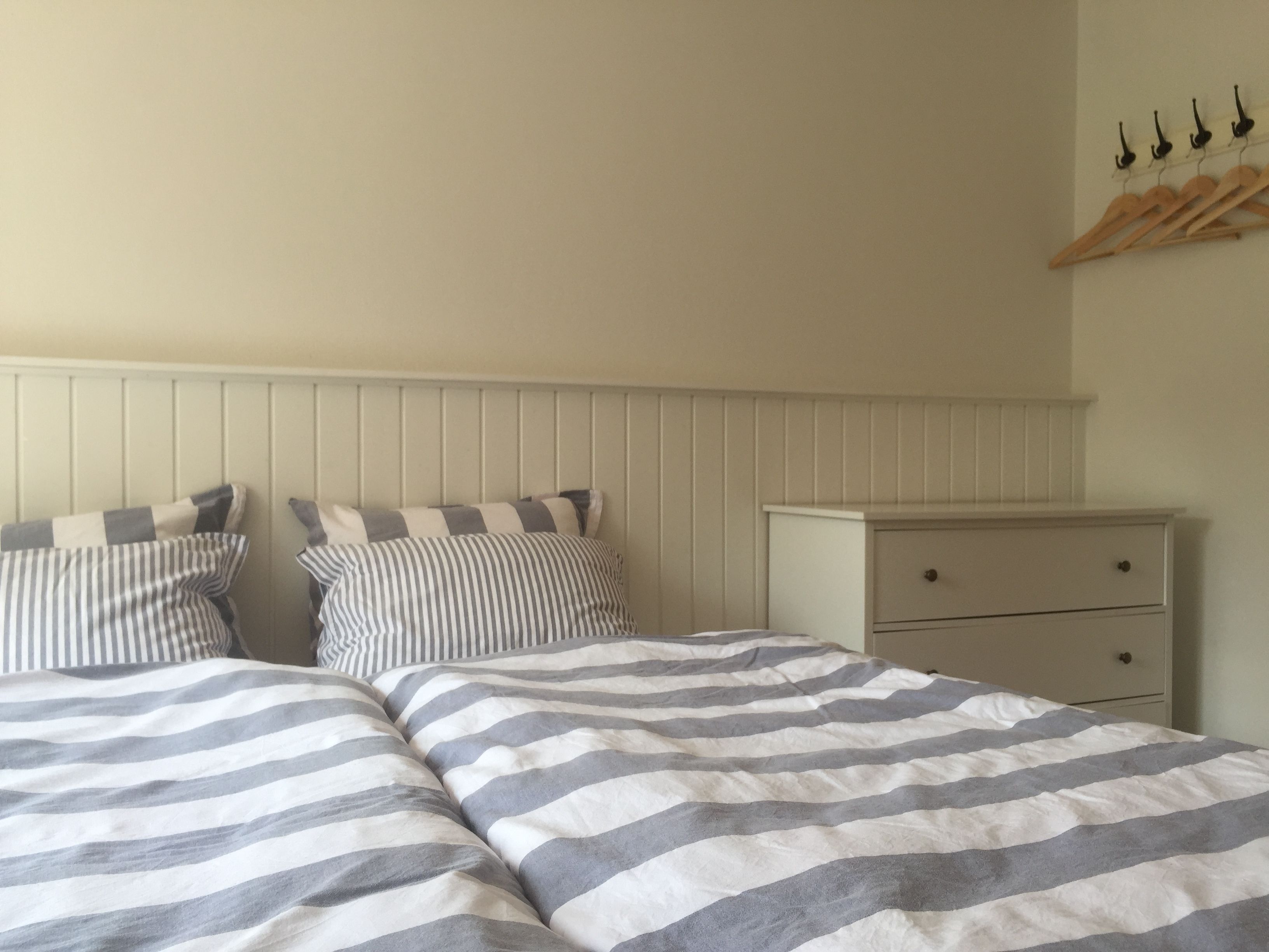 A bedroom with two beds, striped bedding, a wooden dresser, and a wall-mounted coat rack.