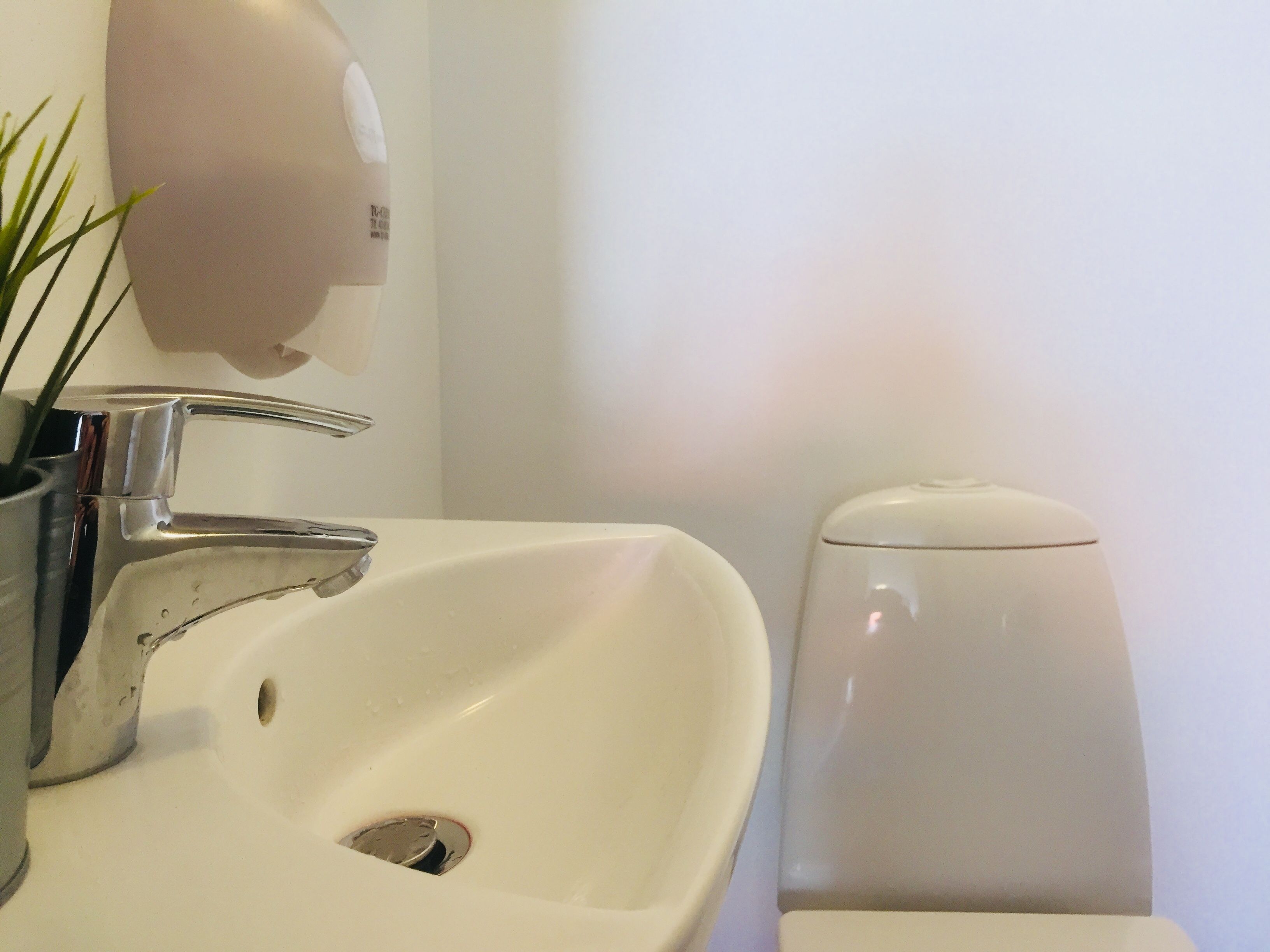 A white bathroom sink with a chrome faucet, a soap dispenser, and a toilet.