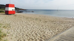 A beach with a red and white lifeguard tower, a wooden walkway, and calm sea with boats.