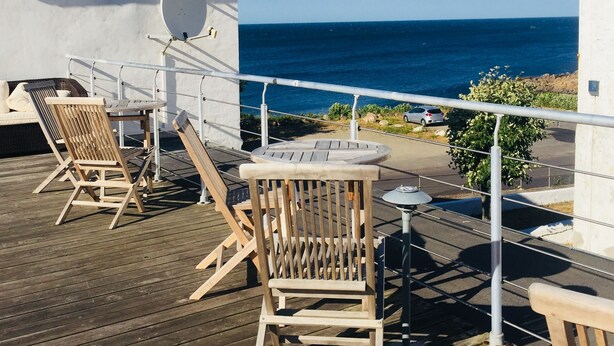 A wooden deck with two wooden chairs and a small round table, overlooking a body of water.