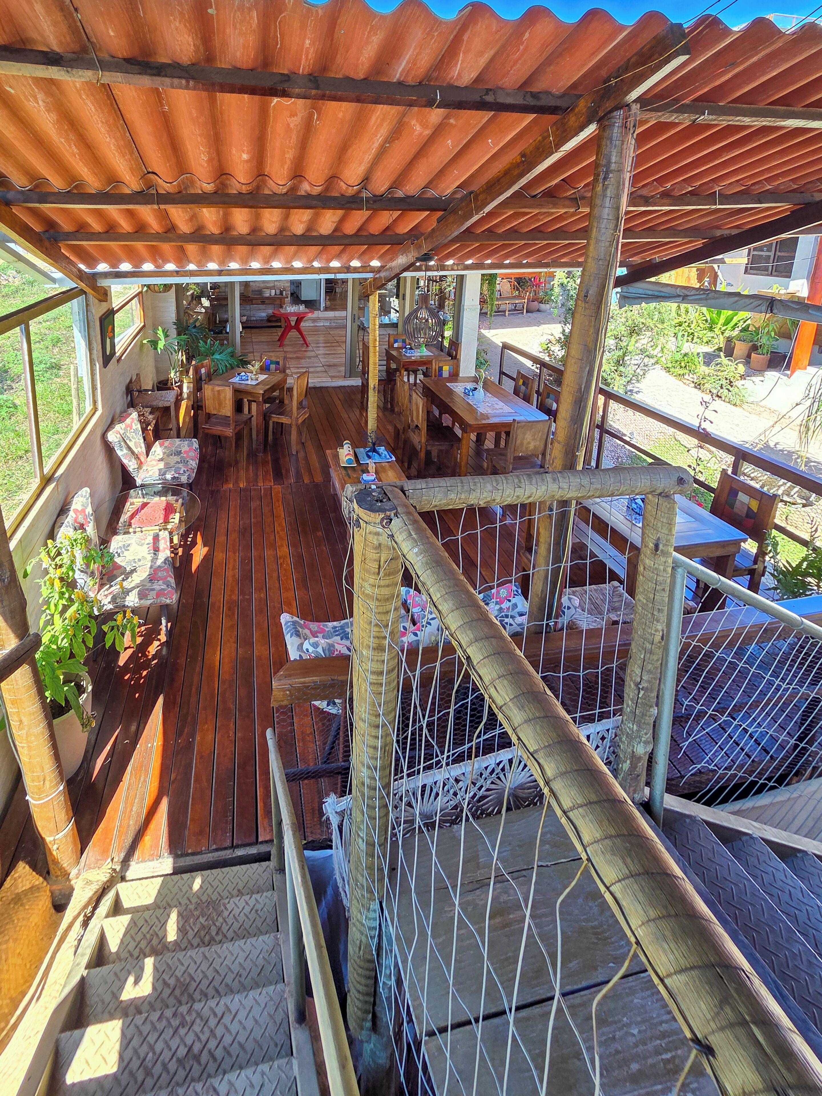 Un espacio de estar al aire libre cubierto, con mesas y sillas de madera, una escalera y vistas del paisaje circundante.