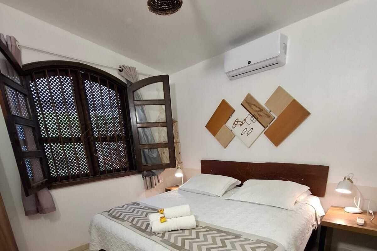 A neatly arranged bedroom with a bed, bedside tables, a hanging light fixture, and a window with a decorative screen.
