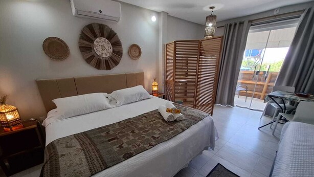 Habitación de hotel con una cama grande, un escritorio con silla, balcón con vistas y ventilador de techo.