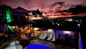 Vista nocturna de un área de piscina en la azotea, con una vista despejada del horizonte de la ciudad y un atardecer.