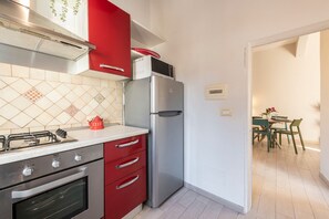 A kitchen with a gas stove, oven, red cabinets, a stainless steel refrigerator, and a microwave on top. - Alfani Terrace (Florence)