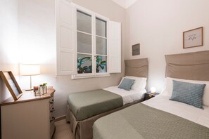 A bedroom with two beds, a window with a view of plants, a bedside table with a lamp, and a wall with framed pictures. - Alfani Terrace (Florence)