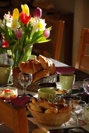 A table set with croissants, bread, a glass of wine, and a vase of tulips. - La Monèze Basse (Malras)
