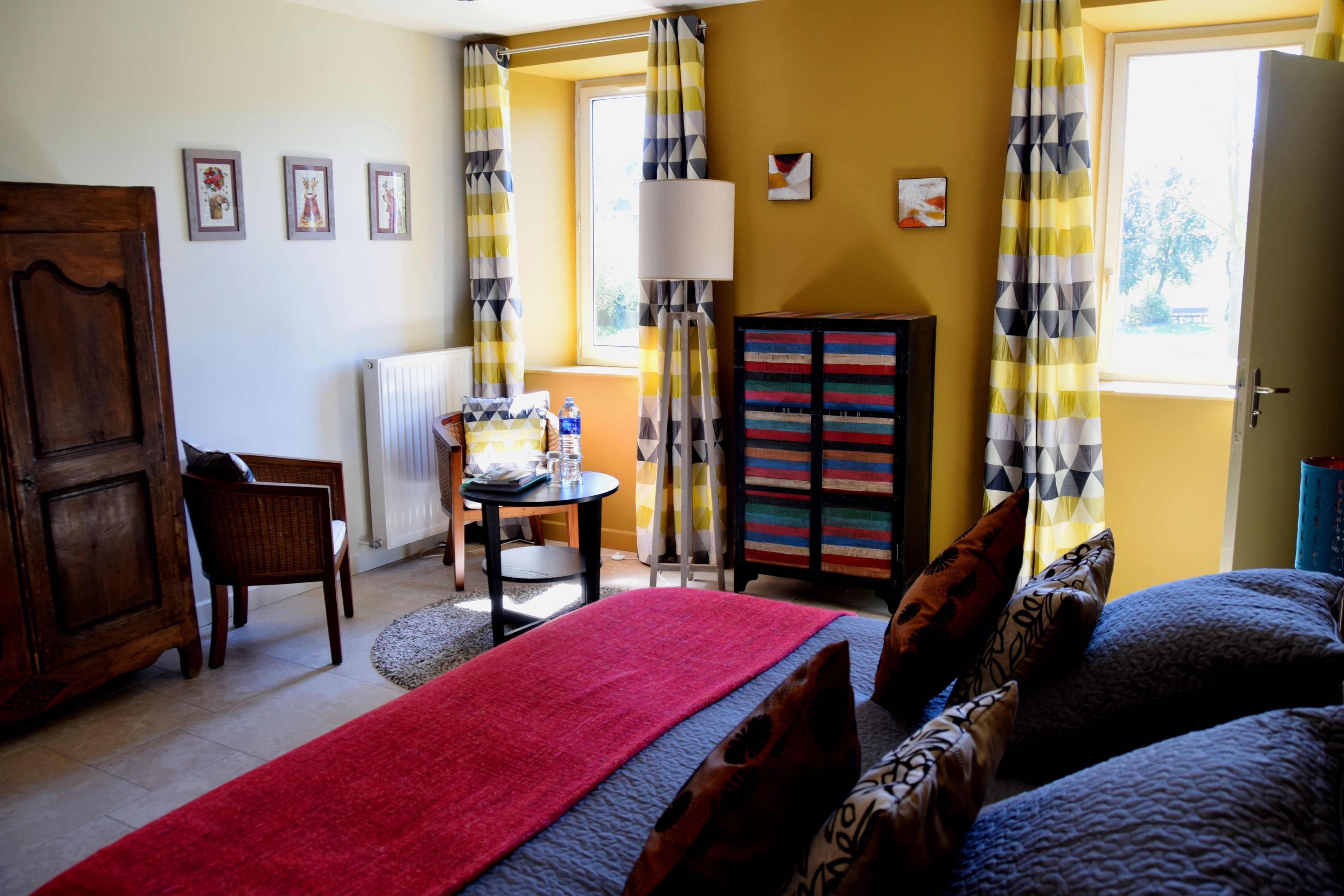 A room with a bed, a chair, a table, a radiator, and a window with curtains.