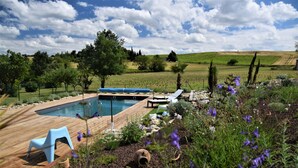 Piscina com deck de madeira, rodeada por um jardim com diversas plantas e flores.