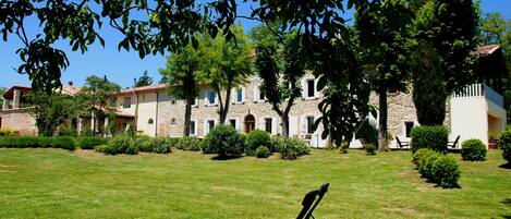 A courtyard with a lawn, a black chair, and a stone building with multiple windows and doors.