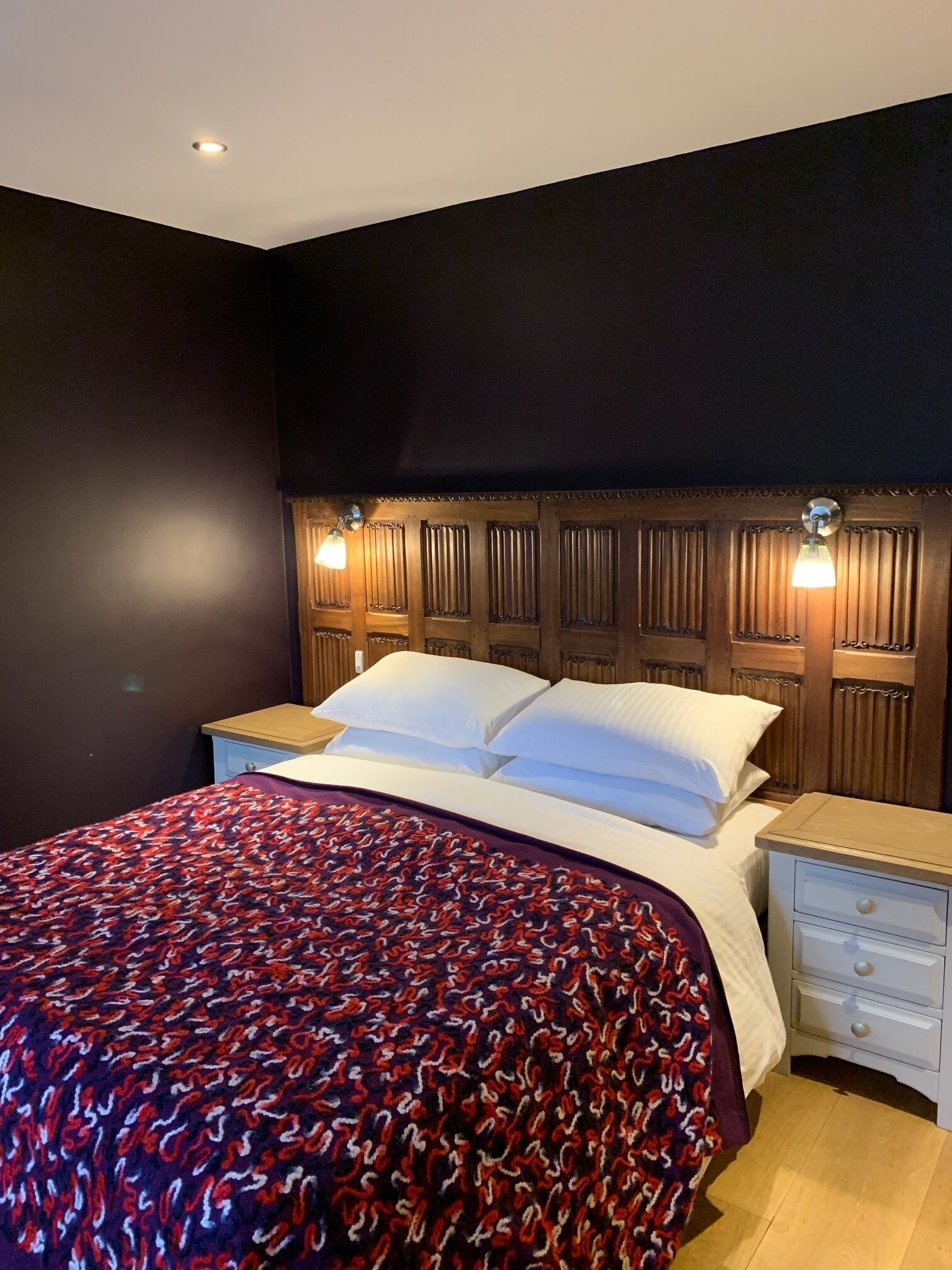 A hotel room with a large bed, two bedside tables, and a dark headboard with vertical slats.