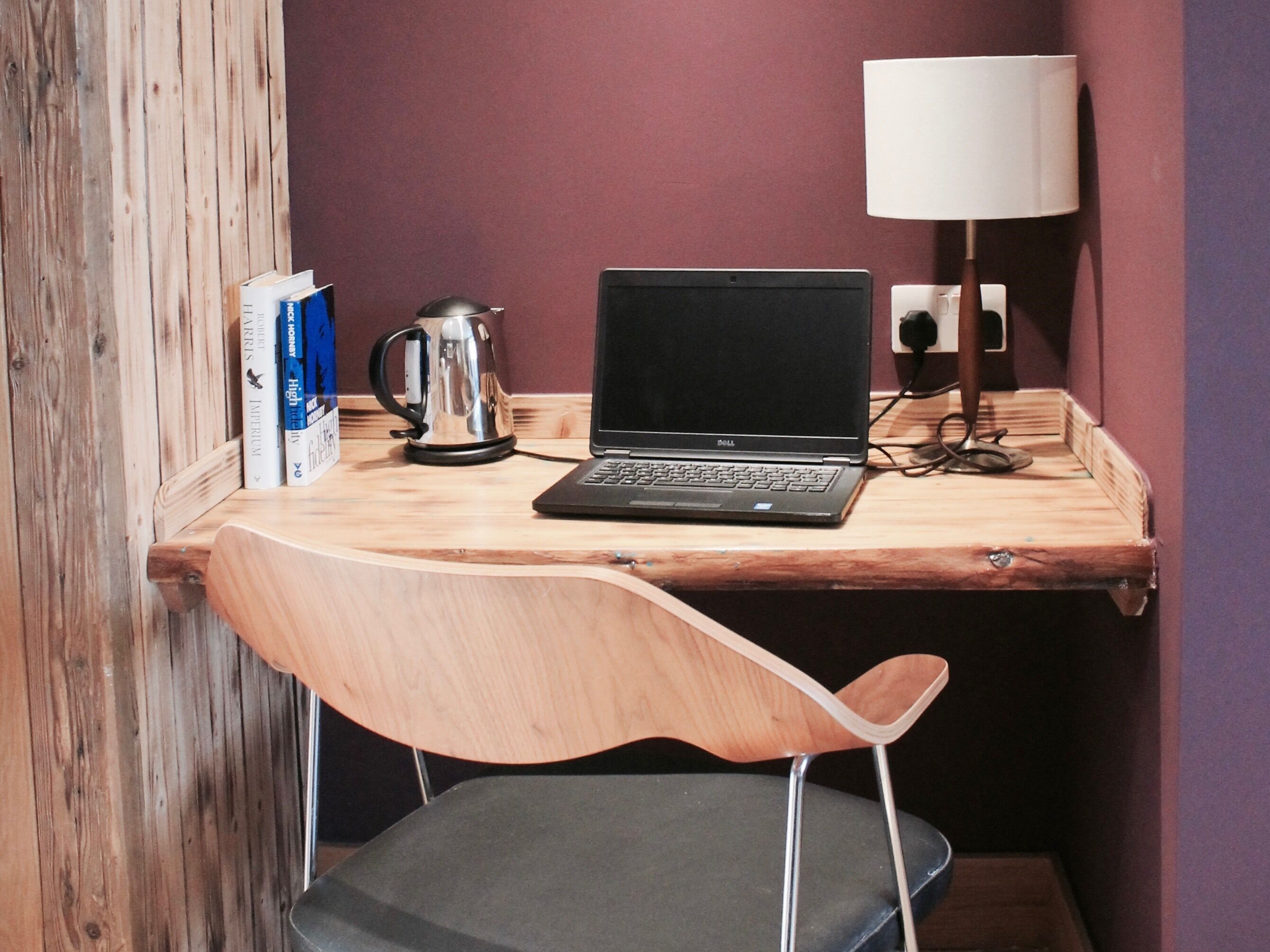 A wooden desk with a laptop, a kettle, and books.