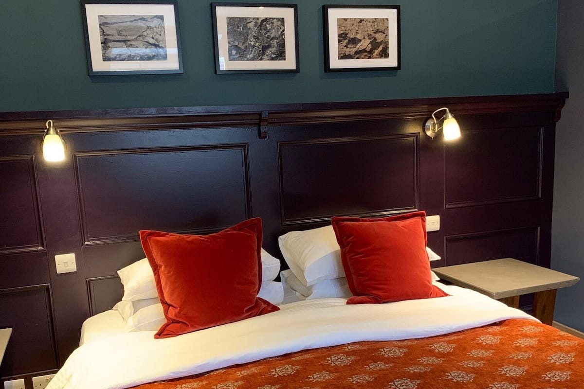 A bed with a patterned red bedspread, two red pillows, a dark headboard, and three framed pictures on the wall.