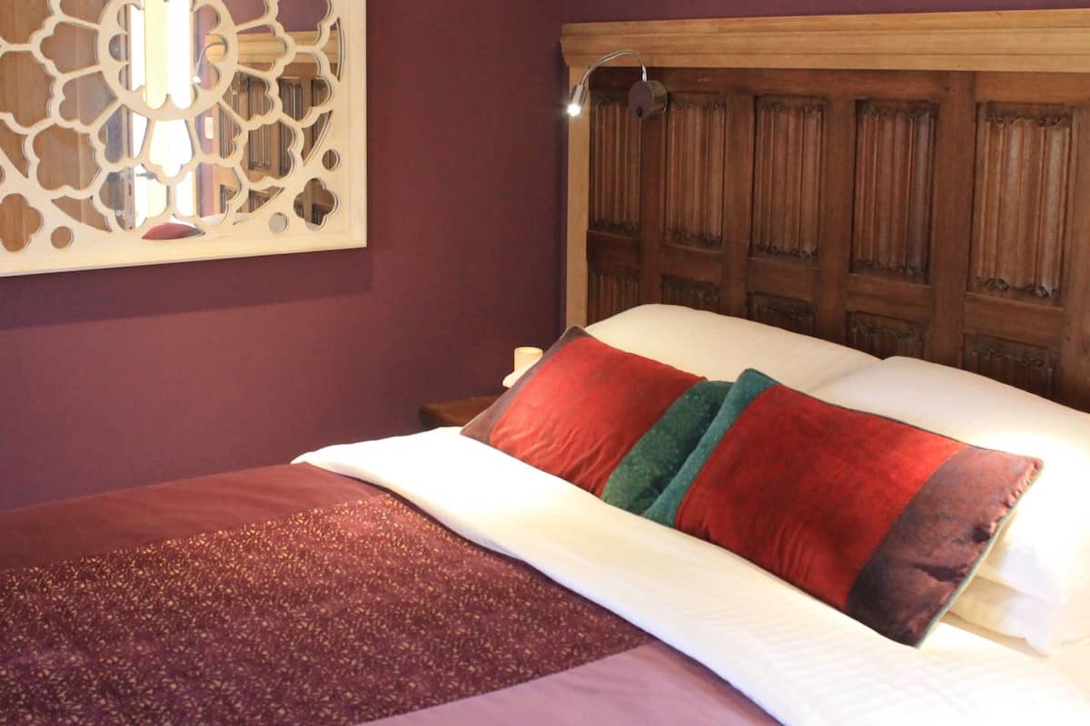 A bed with red and green pillows, a wooden headboard, and a decorative wall piece.