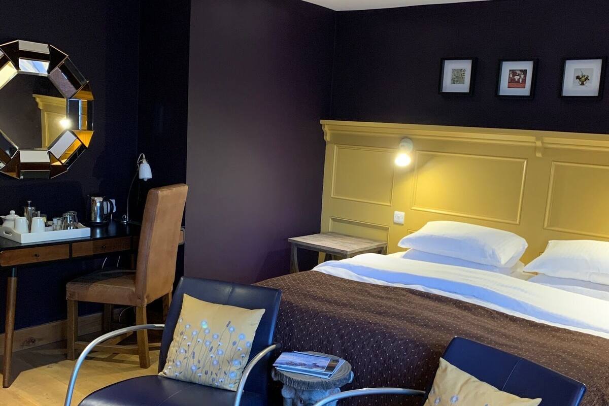 A hotel room with a bed, two chairs, a desk, a mirror, and a nightstand.