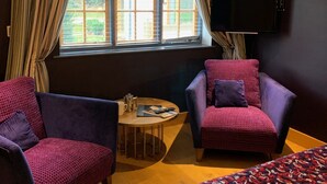 Una camera d'albergo con due poltrone, un tavolino con una caffettiera e un letto con coperta fantasia.