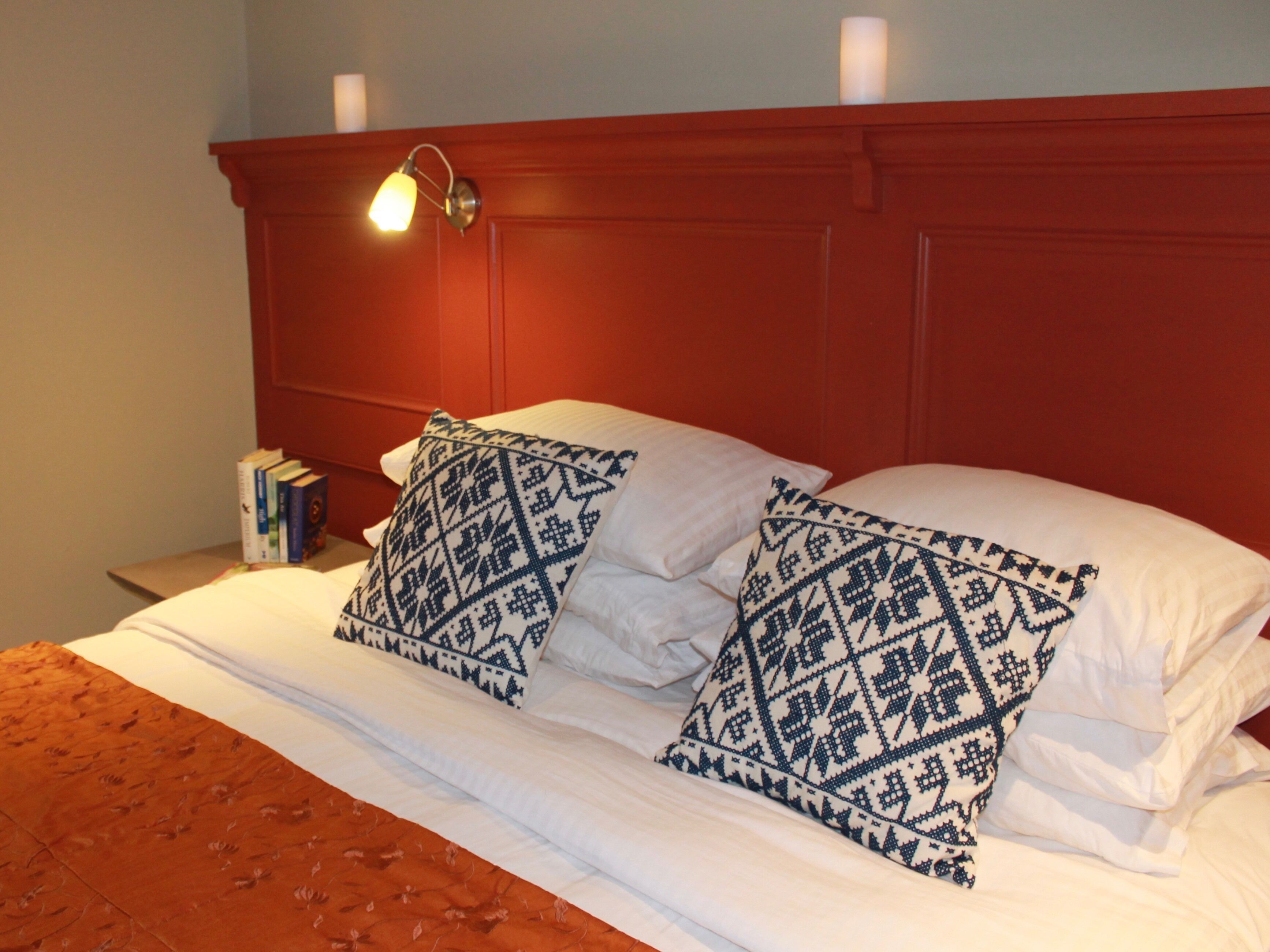 Un lit avec du linge de lit blanc et des oreillers à motifs, une tête de lit rouge et une table de chevet avec des livres.