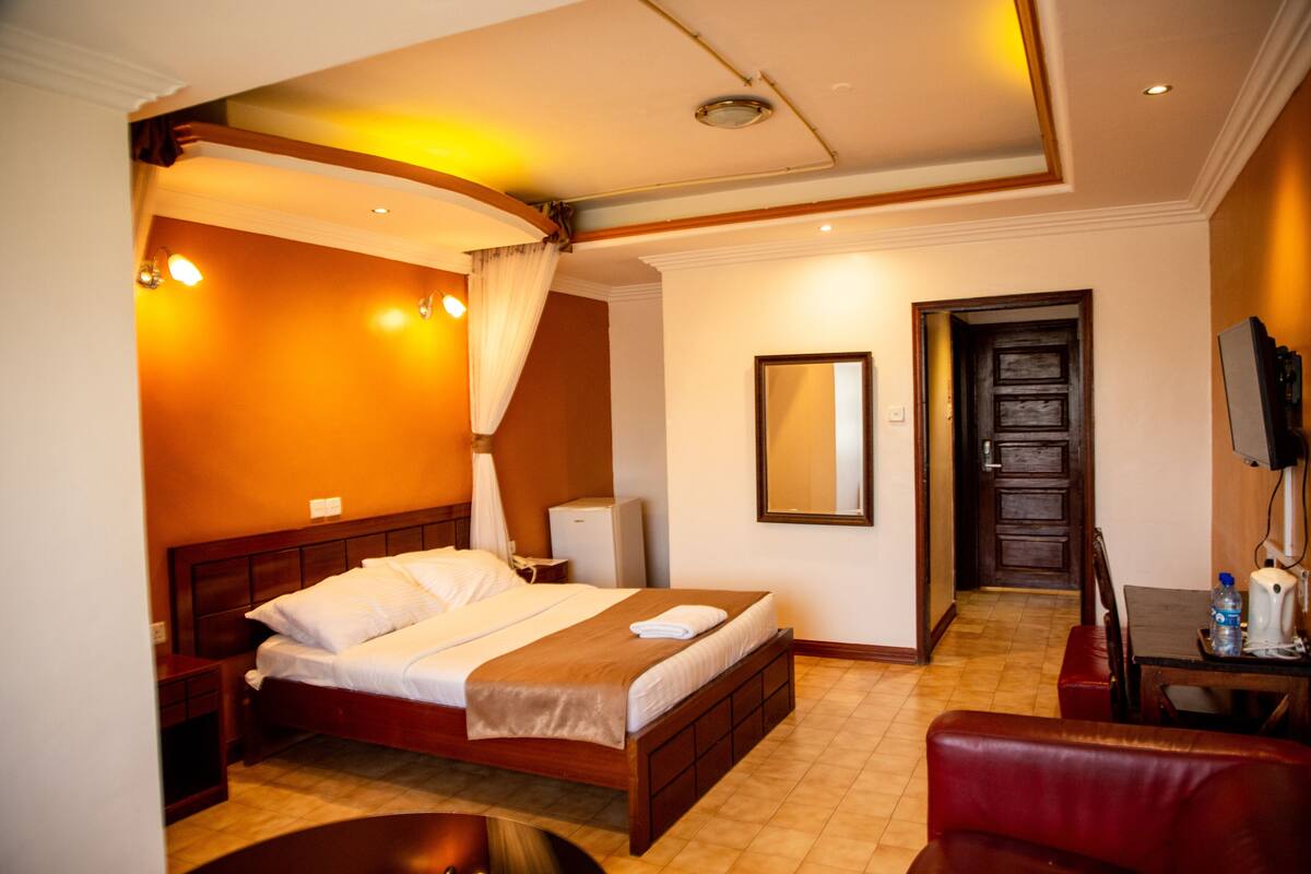 A hotel room with a bed, bedside table, lamp, and a mirror on the wall.