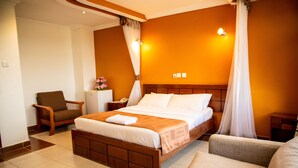 Ein Hotelzimmer mit einem großen Bett, einem Sessel, einem Nachttisch und einem kleinen Tisch.