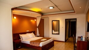 Ein Hotelzimmer mit einem großen Bett, einem Nachttisch aus Holz, einem Spiegel und einem Schreibtisch mit Stuhl.