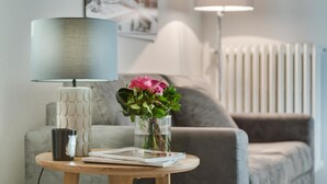 A modern living room with a round wooden table, a lamp, a vase with flowers, and a couch. - Alfani Views (Florence)