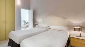 A hotel room with two beds, a bedside table with a lamp, a wardrobe, and a door leading to a bathroom. - Alfani Views (Florence)