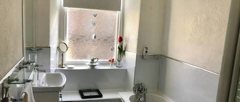 Ein Badezimmer mit Fenster, Waschbecken, Spiegel, Badewanne und Handtuchhalter.