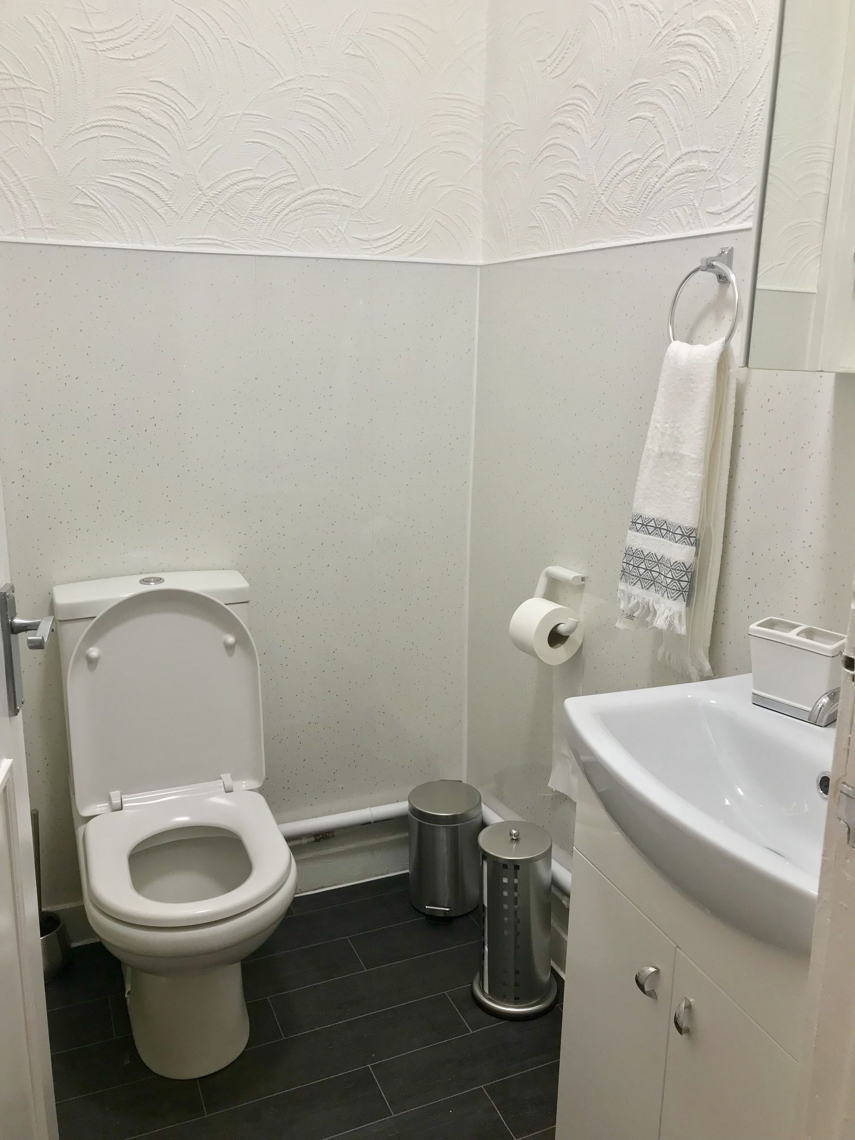 A bathroom with a toilet, a trash can, a sink, and a towel hanging on the wall.