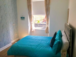 A bedroom with a blue bedspread, a wooden headboard, and a window with curtains. - 233 Leith Apartment (Edinburgh)
