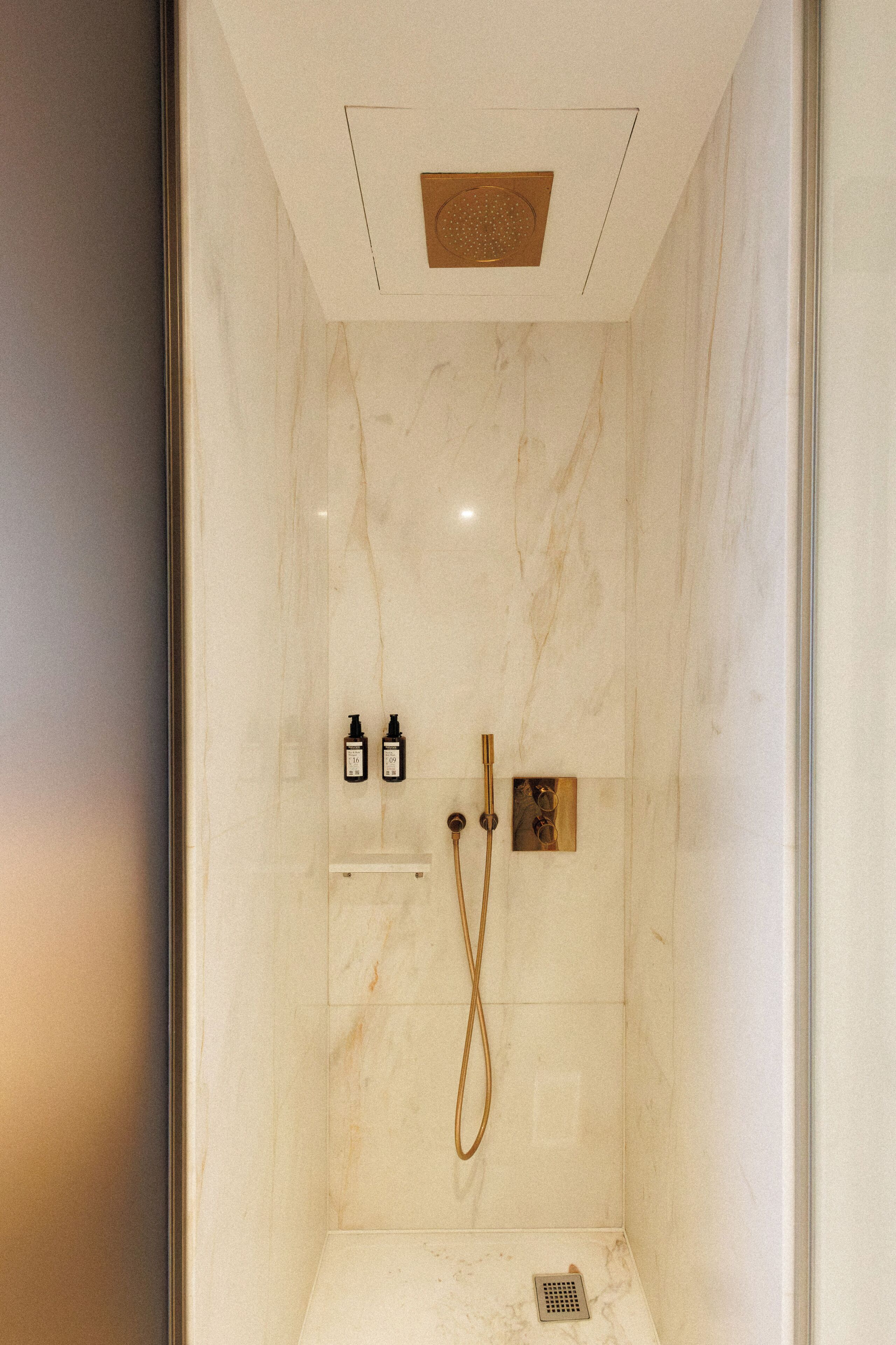 Une douche moderne avec un mur en marbre, un pommeau de douche à main et deux bouteilles de shampoing.