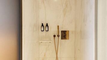 Une douche moderne avec un mur en marbre, un pommeau de douche à main et deux bouteilles de shampoing.