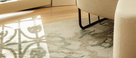 Una habitación con un sillón color crema, una alfombra estampada y un par de sandalias en el suelo.