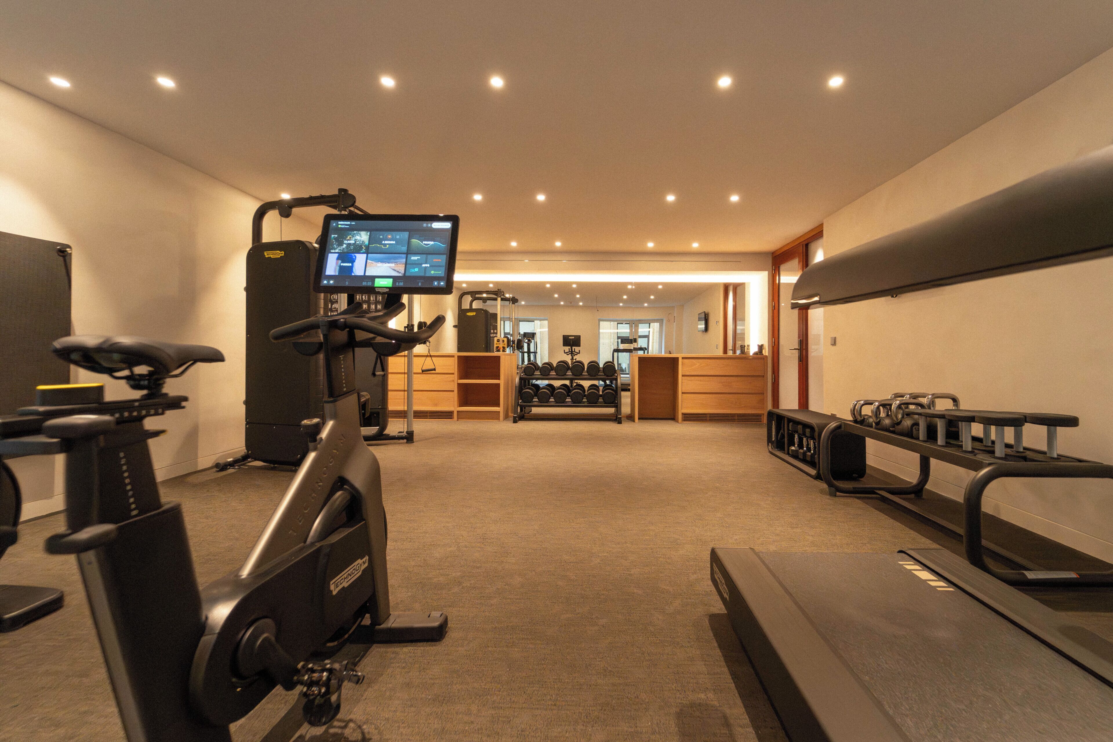 Un gimnasio con equipo cardiovascular, máquinas de pesas y una pantalla digital.