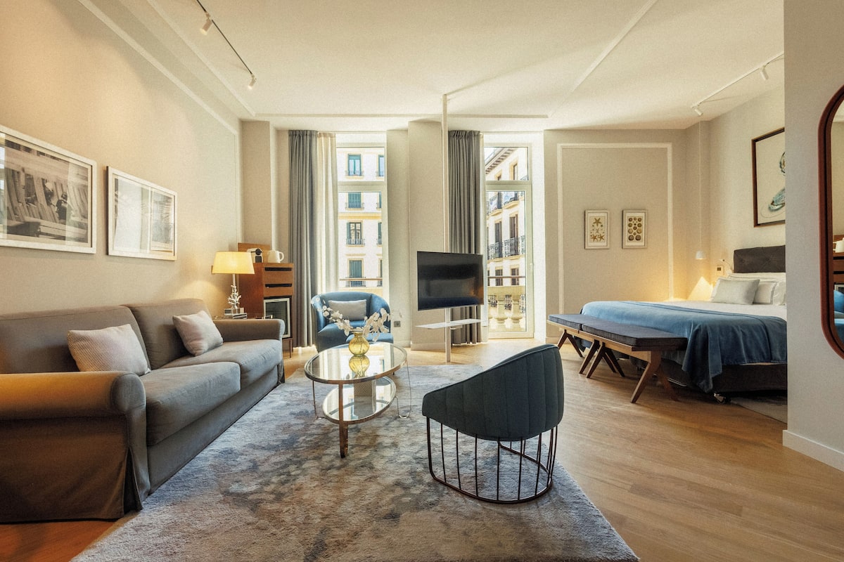 A modern living room with a sofa, a coffee table, a TV, and a bed.
