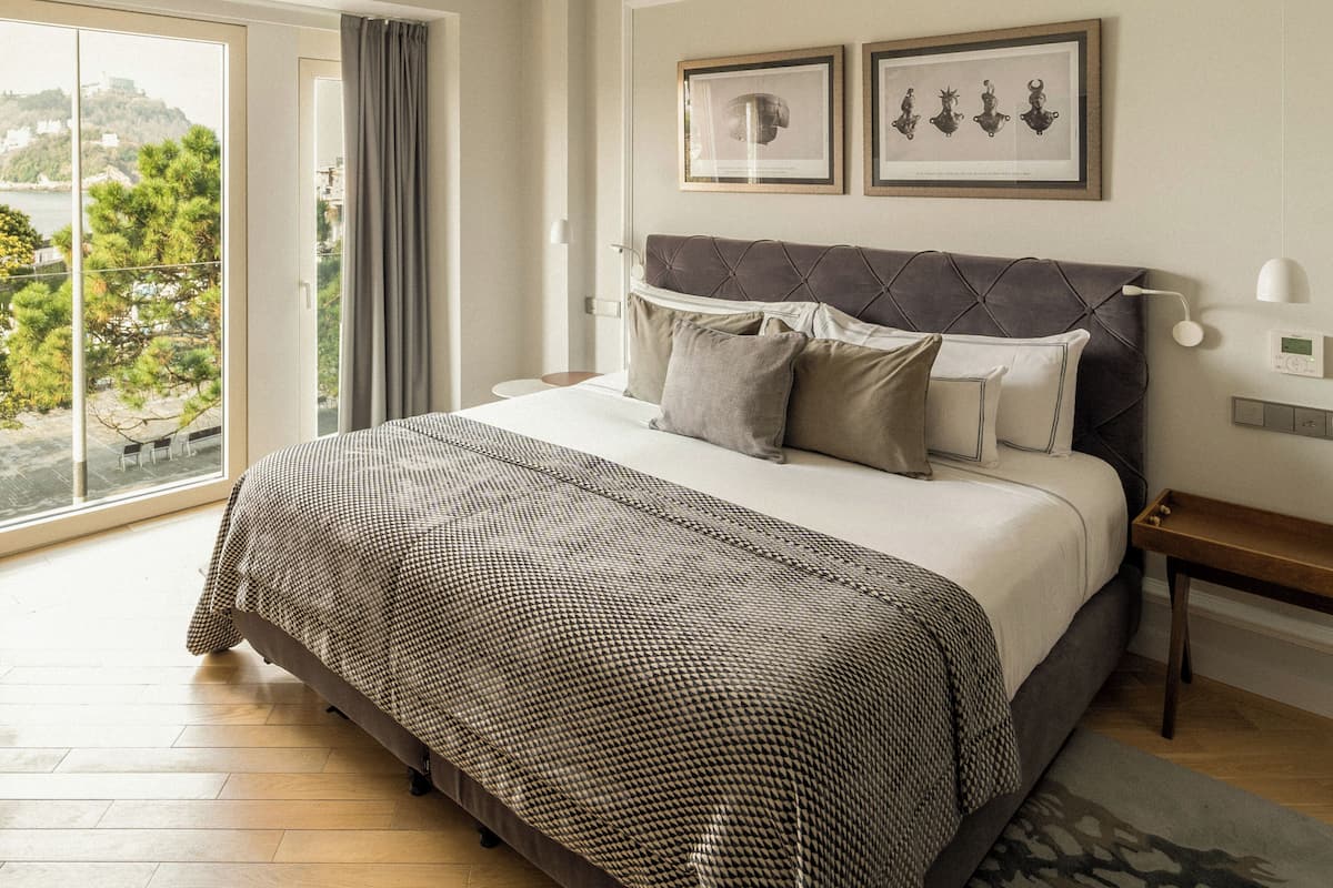 A bedroom with a large bed, a view of a cityscape, and a ceiling with recessed lighting.
