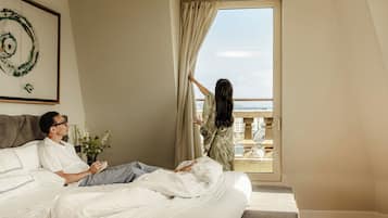 Un dormitorio con cama, ventana con cortinas, un cuadro en la pared y una planta en maceta.