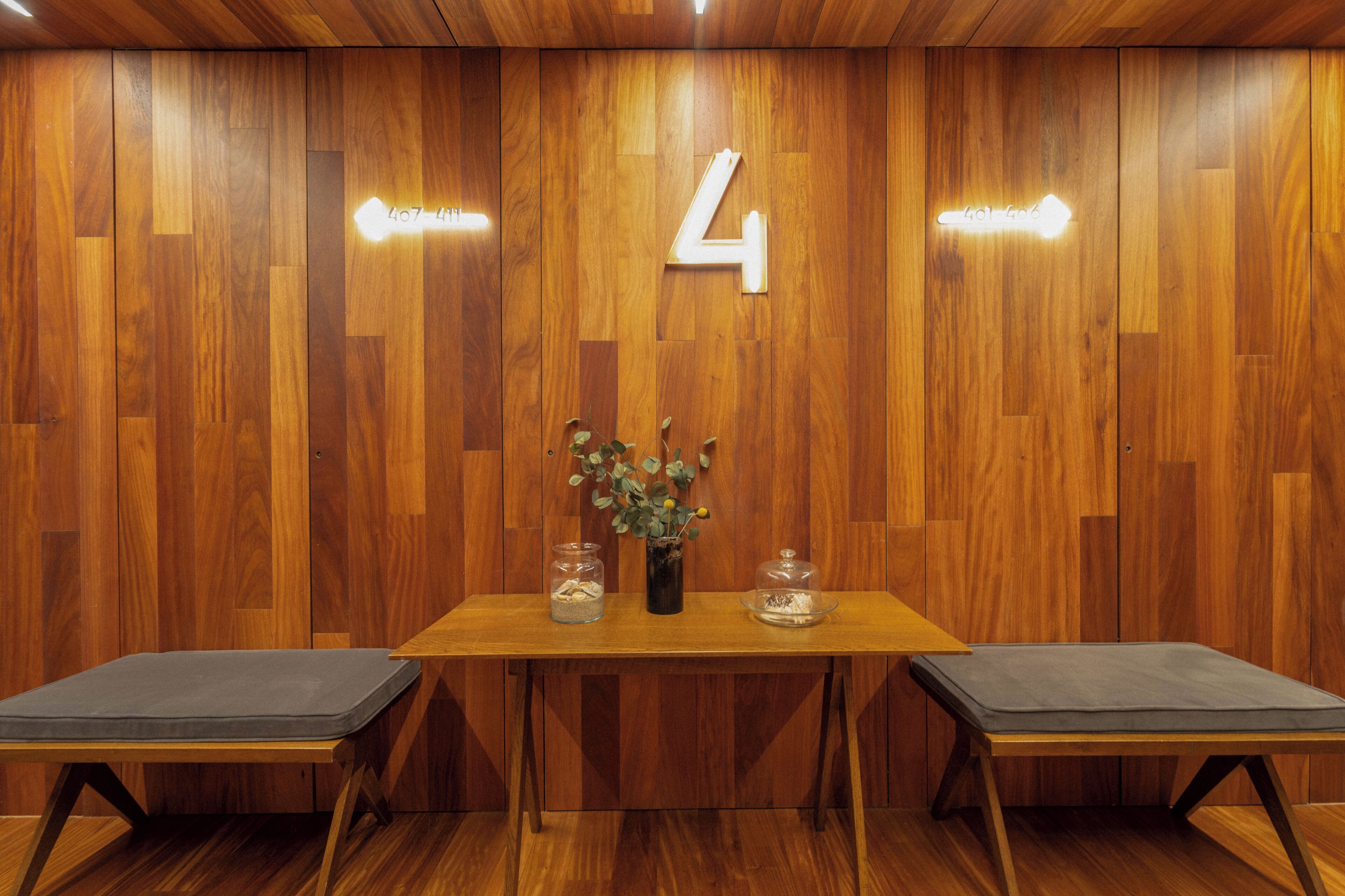 Un mur en bois avec un panneau portant le chiffre « 4 », une table avec un vase et des bocaux en verre, et deux bancs rembourrés.
