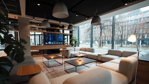 A modern hotel lobby with a large TV screen, comfortable seating, and large windows offering a view of the city. - Q Hotel Plus Wroclaw (Wroclaw)
