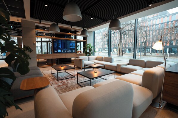 A modern hotel lobby with a large TV screen, comfortable seating, and large windows offering a view of the city. - Q Hotel Plus Wroclaw (Wroclaw)