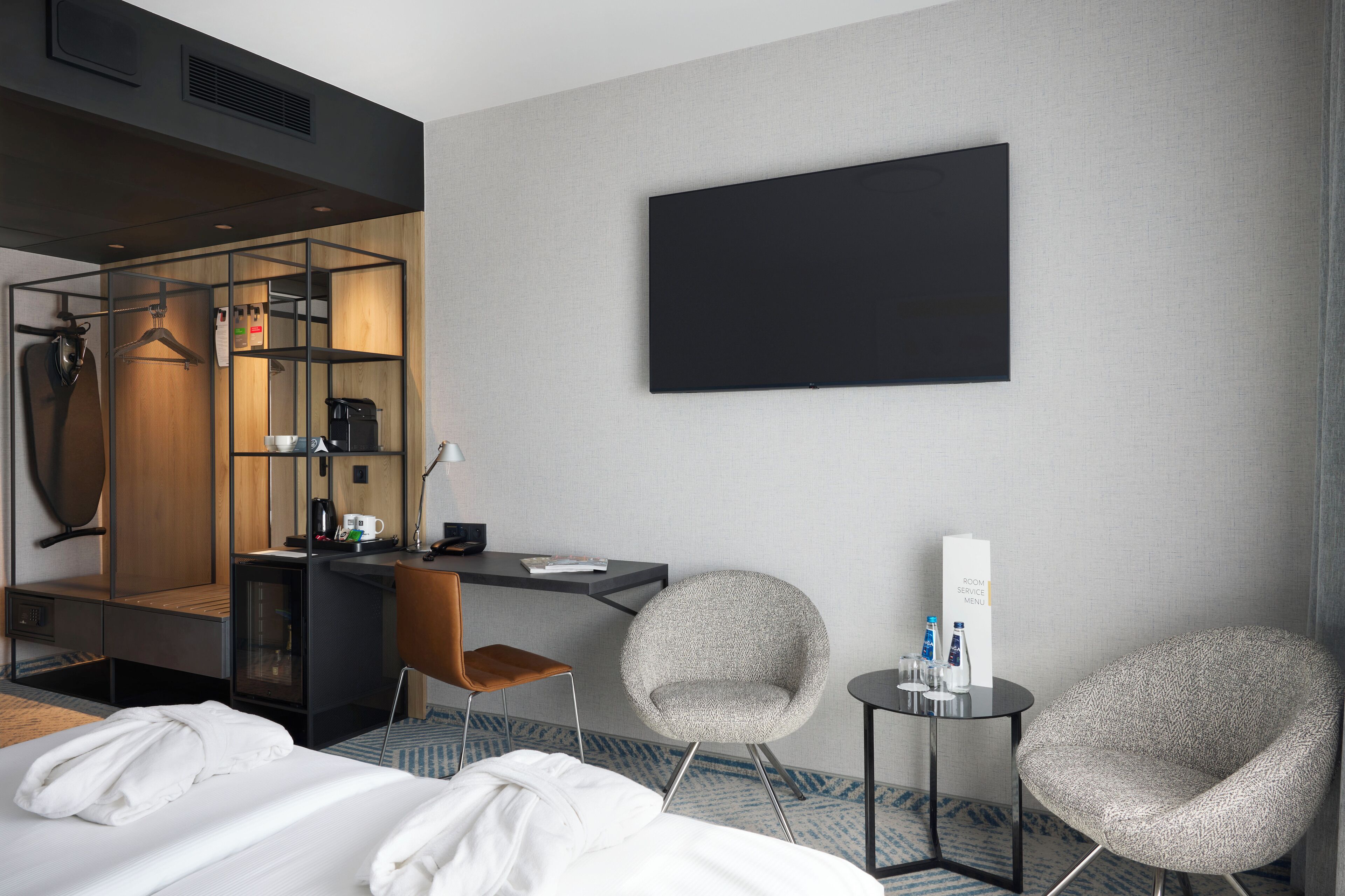 Una habitación de hotel con una cama, un escritorio, dos sillas, un televisor y un espejo.