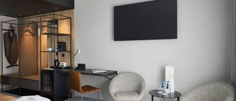 Una habitación de hotel con una cama, un escritorio, dos sillas, un televisor y un espejo.