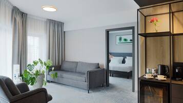 Een moderne hotelkamer met een grijze bank, een tafeltje met een koffiezetapparaat en een potplant.