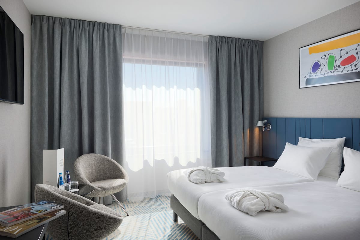 A hotel room with a large bed, a chair, a nightstand, and a window with curtains.
