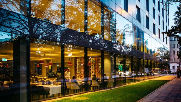 A modern building with a glass facade reflecting trees and sky. Inside, there are tables and chairs arranged for dining. - Q Hotel Plus Wroclaw (Wroclaw)